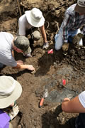 Red flags mark the spots where dense objects were located under the surface. The blue-grey clay layer seen next to the trowel and the red flag is the same material in which other bones have been found.